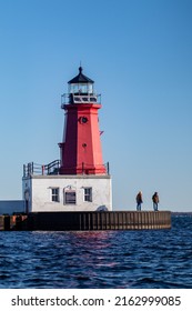 Menominee, Michigan, USA, May, 7, 2022 - Menominee Pierhead Lighthouse "Menominee (Marinette) North Pierhead Light" on the waters of Lake Michigan and the Menomenee River with people fishing, vertical