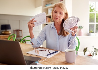 Menopausal Mature Woman Having Hot Flush At Home Cooling Herself With Fan Connected To Laptop - Shutterstock ID 2180443267