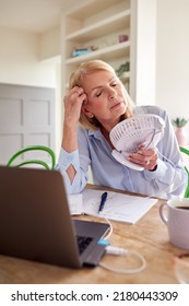 Menopausal Mature Woman Having Hot Flush At Home Cooling Herself With Fan Connected To Laptop - Shutterstock ID 2180443309