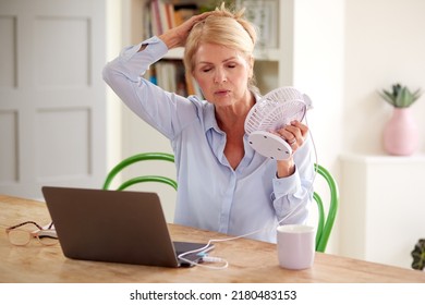 Menopausal Mature Woman Having Hot Flush At Home Cooling Herself With Fan Connected To Laptop - Shutterstock ID 2180483153