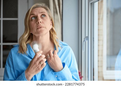 Menopausal Mature Woman Having Hot Flush At Home Cooling Herself With Handheld Electric Fan 