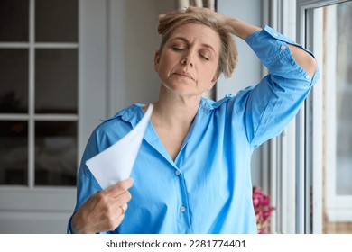 Menopausal Mature Woman Having Hot Flush At Home Cooling Herself With Letters Or Documents