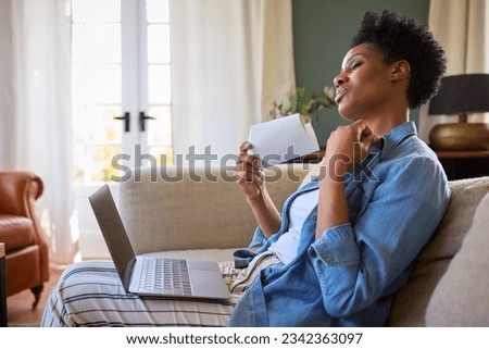 Menopausal Mature Woman At Home With Laptop Having Hot Flush Fanning Herself