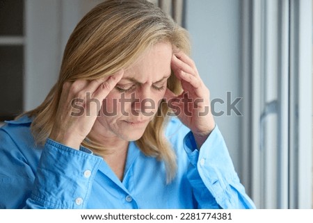 Menopausal Mature Woman At Home Standing By Window Suffering With Headache Or Migraine Pain
