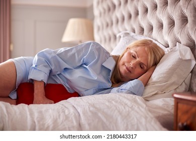 Menopausal Mature Woman Lying In Bed With Hot Water Bottle At Home