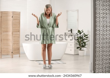 Menopause, weight gain. Concerned woman standing on floor scales in bathroom