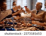 Menorah with lit candles on dining table with extended family toasting in the background on Hanukkah.