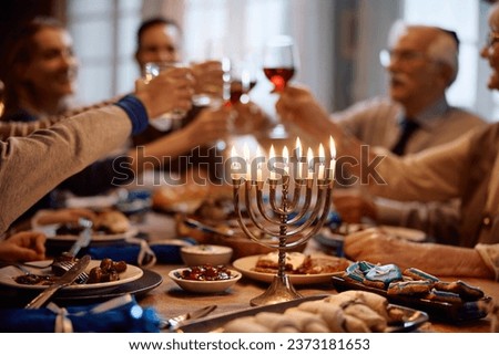 Menorah with lit candles on dining table with extended family toasting in the background on Hanukkah.