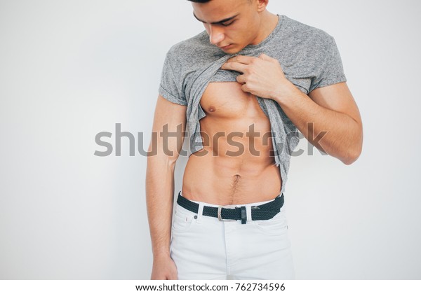 男性の腹筋を押す 運動後の体 ジムの後の男 白い下着を着たセクシーな男 おなかを見る魅力的なスポーツマン 理想的な筋肉と美しい姿 の写真素材 今すぐ編集