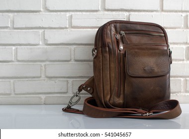 Men's accessories with brown leather bags on wooden table over wall background.