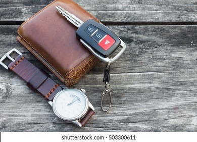 Men's accessories with old brown leather wallet, car key and watch on rustic wooden background