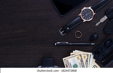 Men's Accessories On A Dark Wooden Background . The Concept Of Success And Business. Wrist Watch, Pen, Perfume, Headphones, Ring, Car Keys, Money And Phone. Flatlay. Copy Space.