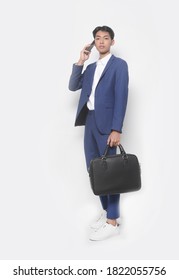 Men's beauty, fashion. Handsome full body young businessman wearing,white shirt and blue pants with sneakers shoes using cellphone holding handbag