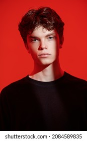 Men's Beauty, Hairstyle. Portrait Of A Guy With Wavy Dark Brown Hair With A Sad, Tired Look And A Beam Of Light On His Face. Studio Shot On A Red Background. Emotions.