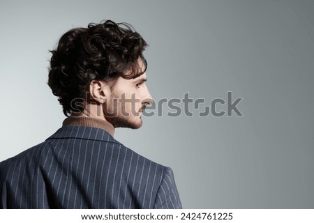 Men's beauty and style. Portrait from the back of a handsome brunette with curly hair in a classic suit. Men's hairstyles. Gray studio background with copy space.