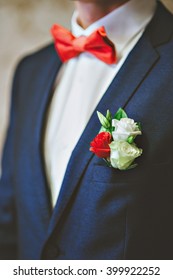 men's blue suit, red tie, white shirt. The groom adjusts his boutonniere of roses