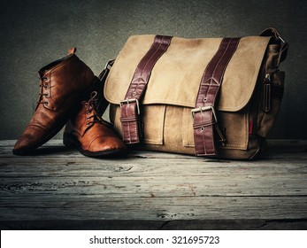 Men's boots and brown bag on wooden table over wall grunge background