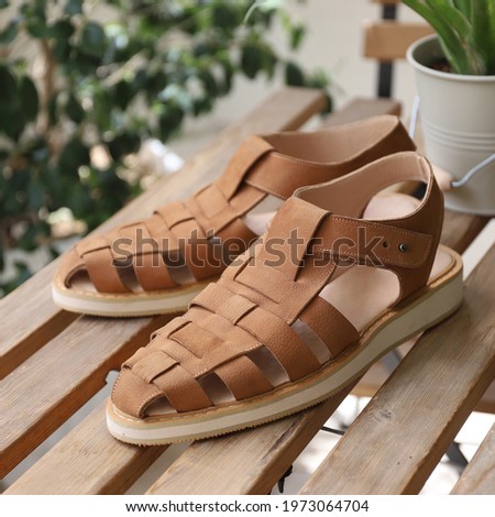 Men's brown leather sandals for summer near green leaves on wooden table - casual style