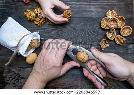 Men's and children's hands at a wooden table crack walnuts. Wooden background with walnuts and hands.