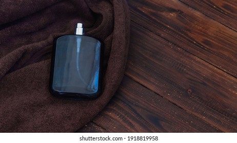 Men's Cologne In A Black Glass Bottle On A Brown Terry Towel And A Wooden Table.