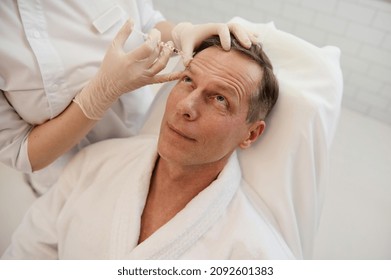 Men's cosmetology. Beautician injects a botulinum toxin into a man's forehead to relax the muscles. Mature man receiving facial rejuvenation injection procedure for smoothing and anti-aging therapy