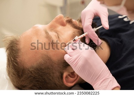 Men's cosmetology. Cosmetologist makes botulinum toxin beauty injection procedure to man in wrinkles near eyes of rejuvenation of handsome young man with beard in beauty salon.