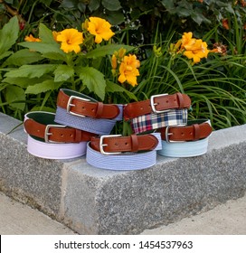 Men's Fabric Seersucker Gingham Madras Pattern Leather Tab Belts In Front Of Flowers And Plants For A Summer Background.