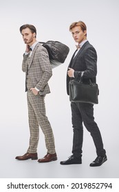 Men's Fashion And Accessories. Full Length Portrait Of Two Elegant Young Men In Classic Three-piece Suits Holding Leather Bags On A White Background.