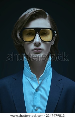 Men's fashion and style. A well-groomed young man with stylish hair styling, posing in an elegant black classic suit, white shirt, a tie and big sunglasses. Black background.