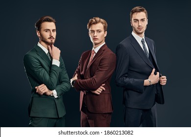 Men's fashion. Three handsome men in elegant suits posing together on a dark blue background. Male beauty. Studio portrait.