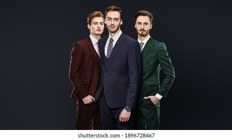 Men's Fashion. Three Handsome Men In Elegant Suits Posing Together On A Dark Blue Background. Male Beauty. Studio Portrait.