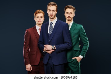 Men's Fashion. Three Handsome Men In Elegant Suits Posing Together On A Dark Blue Background. Male Beauty. Studio Portrait.