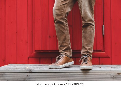 Men's feet in brown sneakers and brown corduroy trousers stand on the porch in front of the front door. The facade of the house is bright red. - Powered by Shutterstock