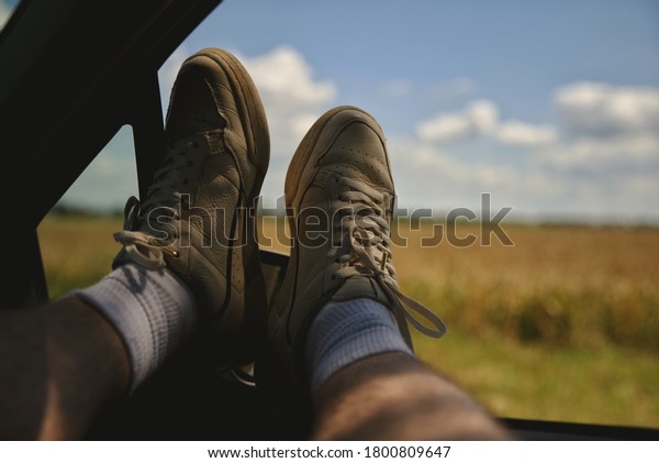 Men\'s feet in the car window on the\
road background. The concept of freedom and\
travel.