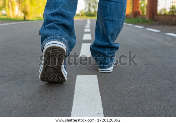 Men\'s feet on the asphalt. A man walks along the\
road markings