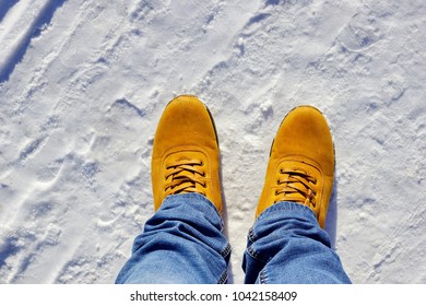 men's feet in orange boots and jeans in the snow - Shutterstock ID 1042158409