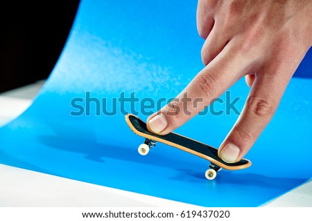Men's fingers are doing the trick on fingerboard against the blue ramp closeup