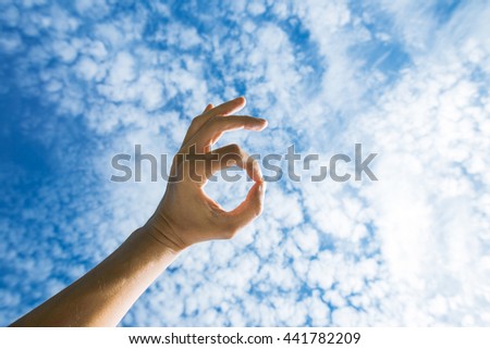 men's hand doing all right sign on the background of sky with clouds