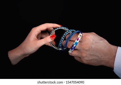 Men's hand giving blue bracelet to woman's hands in a black background - Powered by Shutterstock