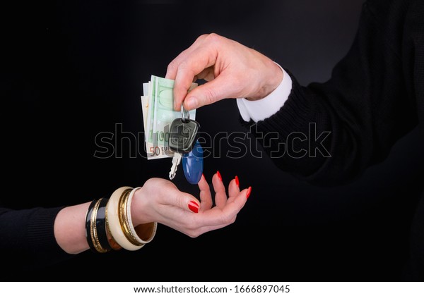 Men\'s hand giving to  woman\'s hand euro\
banknotes and car keys.  Black\
background