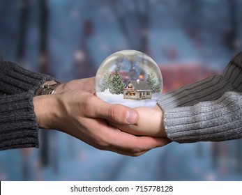 Men's hands and child's hands holding a glass ball. Ball Christmas scenery inside. Fairy house, snow, winter. - Powered by Shutterstock