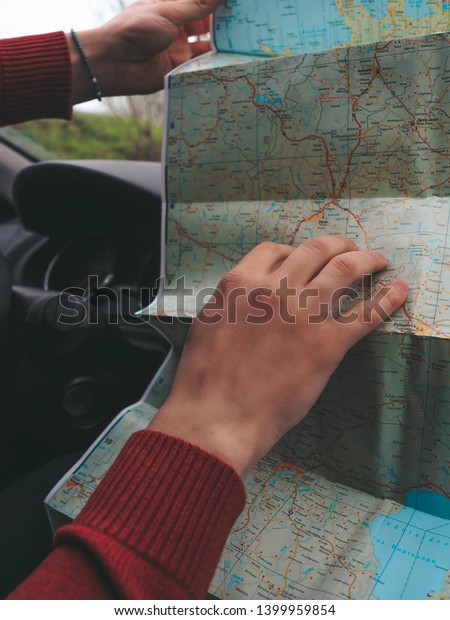 Men\'s hands explore the paper map, spreading it in\
the car