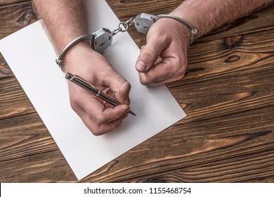 Men's hands with handcuffs fill the police record, confession. on top see the police investigative detective. Arrest, bail, criminal, prison.