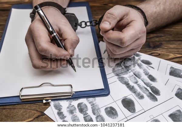 Men\'s\
hands with handcuffs fill the police record, confession. on top of\
the police investigative detective. Arrest, bail, criminal, prison.\
fingerprints, criminalist. the attacker.\
close-up