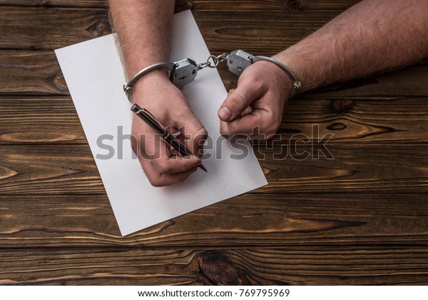 Men\'s hands with handcuffs fill the police\
record, confession. on top see the police investigative detective.\
Arrest, bail, criminal,\
prison.