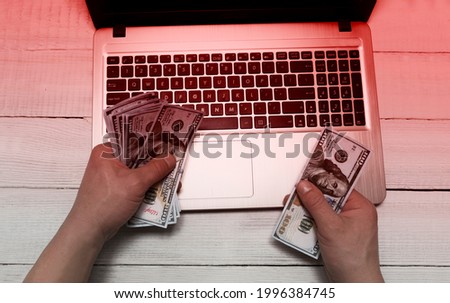 Men's hands hold money dollars against the background of an open laptop. Red toning. The concept of online fraud, internet fraud, deception, extortion of money, debts, online gambling.
