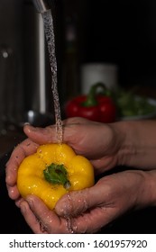 Men's hands are holding big yellow pepper in water jet. Product preparation for home cooking. Shallow depth of field.