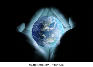 Men's hands holding the planet earth rotated the continents of North and South America with a blue glow on a black background.