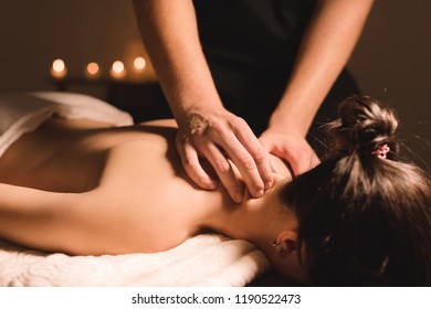 Men's hands make a therapeutic neck massage for a girl lying on a massage couch in a massage spa with dark lighting. Close-up. Dark Key - Shutterstock ID 1190522473