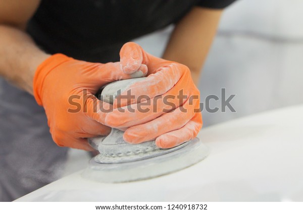 men\'s hands in orange gloves\
polish the hood of a car with a pneumatic polisher in the\
garage\
